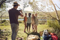 Giovane uomo fotografare gli amici al lungofiume soleggiato estate — Foto stock