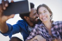 Усміхнена, захоплена багатоетнічна пара бере селфі з телефоном — стокове фото