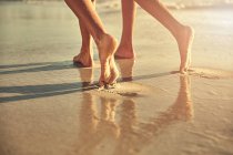 Pés descalços de mulheres andando na areia molhada na praia de verão ensolarada — Fotografia de Stock