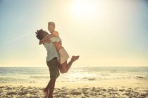Грайливий хлопець піднімає дівчину на сонячному літньому океані пляжу — стокове фото