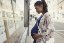 Mujer embarazada navegando anuncios inmobiliarios en escaparate urbano - foto de stock