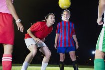 Young female soccer players practicing on field at night, heading the ball — Stock Photo