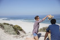 Donna ponendo cappello sul fidanzato sulla spiaggia soleggiata dell'oceano estivo — Foto stock