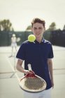 Jovem jogador de tênis do sexo masculino saltando bola de tênis em raquete de tênis no campo de tênis — Fotografia de Stock