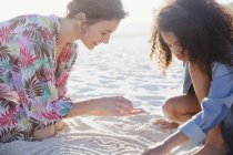 Mother and daughter drawing in sand on sunny summer beach — Stock Photo