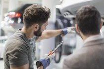 Auto mechanic with tool pointing, explaining to customer in auto repair shop — Stock Photo