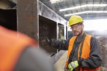 Männlicher Arbeiter gestikuliert, erklärt Stahlteil dem Kollegen in Fabrik — Stockfoto