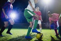 Jeunes joueuses de soccer jouant sur le terrain la nuit, donnant un coup de pied au ballon — Photo de stock
