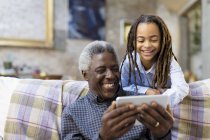 Happy grandfather and granddaughter using smart phone on sofa — Stock Photo