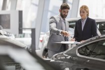 Car sales people meeting, examining new car in car dealership showroom — Stock Photo