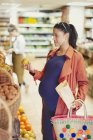 Беременная женщина покупает яблоки в продуктовом магазине — стоковое фото