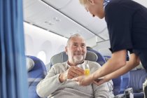 Бортпроводник подает апельсиновый сок человеку в самолете — стоковое фото