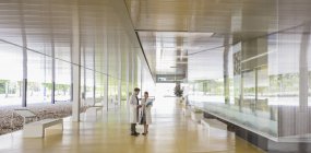 Scientists in lab coats talking in modern office lobby corridor — Stock Photo
