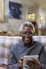 Hombre mayor sonriente usando tableta digital en sofá - foto de stock