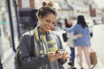 Smiling young woman texting with cell phone on sunny urban street — Stock Photo