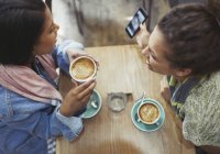 Female friends drinking coffee and using cell phone in cafe — Stock Photo