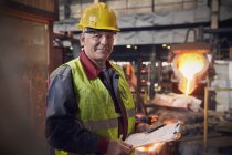Porträt selbstbewusster Stahlarbeiter mit Klemmbrett im Stahlwerk — Stockfoto