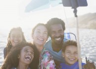 Happy, playful multi-ethnic family taking selfie with selfie stick on sunny summer beach — Stock Photo