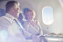 Sorrindo casal maduro comer e falar em primeira classe no avião — Fotografia de Stock