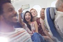Playful young friends with camera phone taking selfie on airplane — Stock Photo