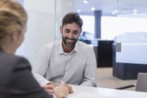 Smiling male customer listening to car saleswoman in car dealership office — Stock Photo