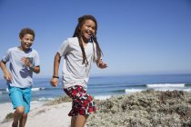 Glückliches Geschwisterpaar läuft am sonnigen Sommerstrand am Meer — Stockfoto