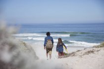 Отец и дочь гуляют с доской на солнечном летнем берегу океана — стоковое фото