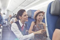 Asistente de vuelo femenina ayudando a chica en el avión - foto de stock
