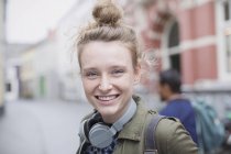 Porträt einer lächelnden jungen Frau mit Kopfhörern auf der Straße der Stadt — Stockfoto