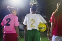 Young female soccer players with ball talking on field at night — Stock Photo