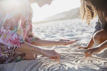Mother and daughter drawing spirals in the sand on sunny summer beach — Stock Photo