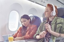 Jeunes amies avec écouteurs et tablette numérique dans l'avion — Photo de stock