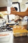 Женщина разбивает свежий перец на яйцах, готовящихся на плите на кухне — стоковое фото