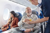 Бортпроводник подает апельсиновый сок человеку в самолете — стоковое фото