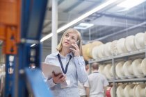 Female supervisor with clipboard talking on cell phone in fiber optics factory — Stock Photo