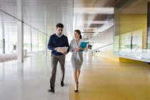 Empresário e empresária caminhando e discutindo papelada no corredor de escritório moderno — Fotografia de Stock