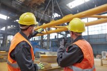 Trabalhadores do sexo masculino assistindo equipamentos sendo levantados na fábrica — Fotografia de Stock