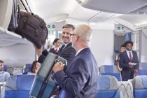 Empresários carregando bagagem em compartimento de armazenamento no avião — Fotografia de Stock
