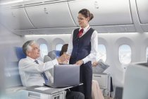 Flight attendant serving drink to businessman working at laptop on airplane — Stock Photo