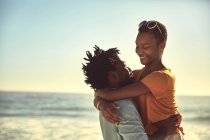 Cariñosa pareja joven abrazándose en la soleada playa de verano - foto de stock