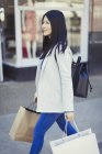 Young woman walking along storefront with shopping bags — Stock Photo
