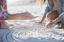 Mutter und Tochter legen Muscheln spiralförmig in den Sand am sonnigen Sommerstrand — Stockfoto