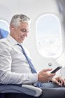 Uomo d'affari che ascolta musica con cuffie e lettore mp3 in aereo — Foto stock