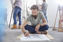 Männlicher Künstler sitzt im Schneidersitz auf dem Fußboden im Atelier des Kunstkurses — Stockfoto
