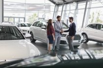 Car salesman and customers handshaking in car dealership showroom — Stock Photo