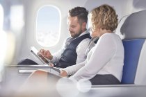 Бизнесмен и предпринимательница используют цифровой планшет в самолете — стоковое фото