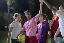 Уверенная в себе молодая женская футбольная команда дает пять на поле ночью — стоковое фото