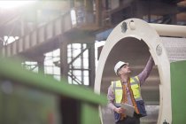 Ingenieur mit Klemmbrett untersucht Stahlrohr in Fabrik — Stockfoto
