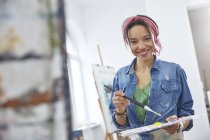 Портрет усміхненої жінки-художниці з пензлем і палітрою, живопис в студії арт-класу — стокове фото