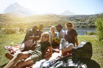 Портрет усміхнених молодих друзів, що зависають, насолоджуючись пікніком на сонячному літньому березі річки — стокове фото
